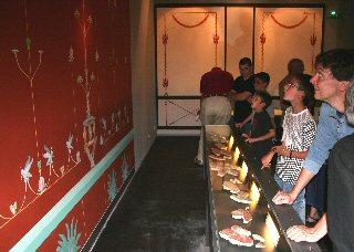 Visiteurs découvrant les peintures murales gallo-romaines restituées, sur fond rouge